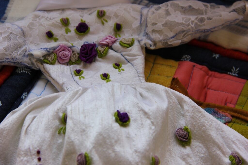 A doll dress with the floral designs we are known for. Also, a neckline with a circle made of violet and pink flowers.