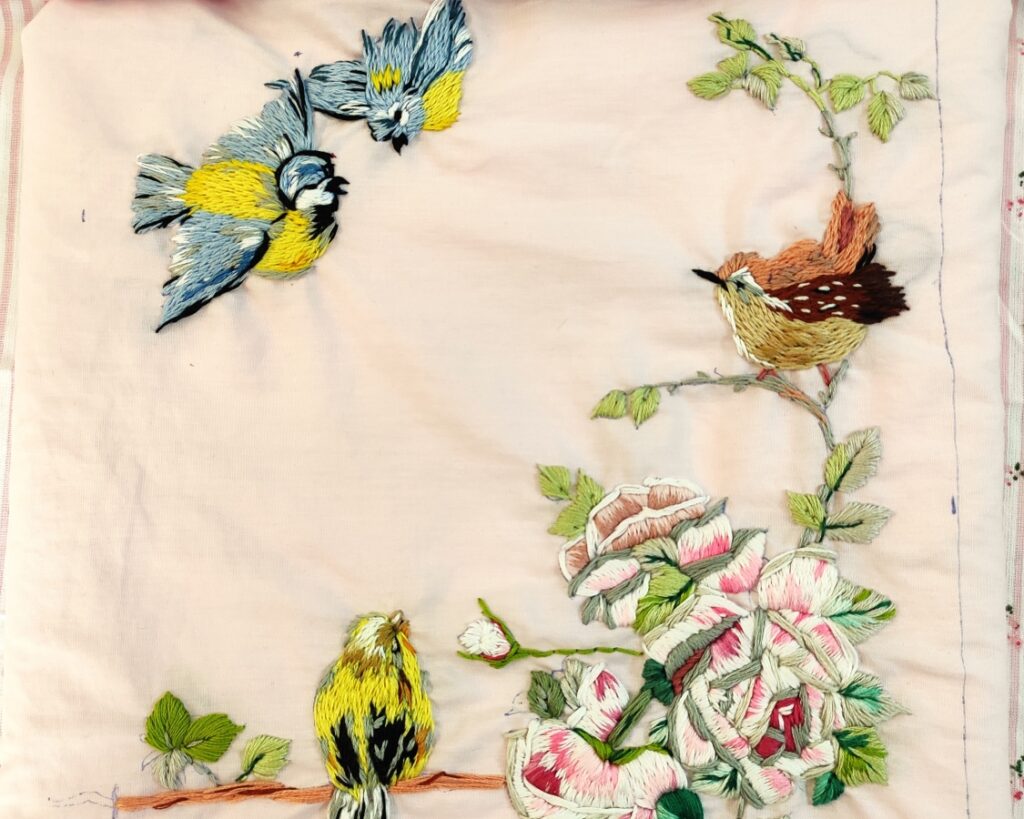 Sparrows hanging onto a tree branch along with flower embroidery work.